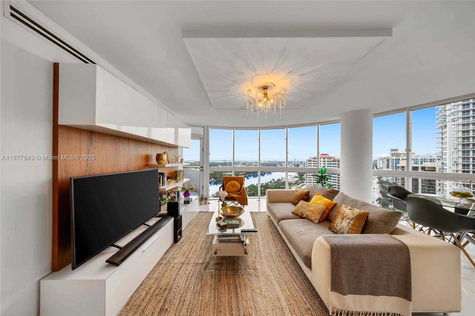 A living room features a large television, a beige sofa, and floor-to-ceiling windows with views — 6301 Collins Ave # 2107, Miami Beach FL 33141, MIAMI BEACH, FL