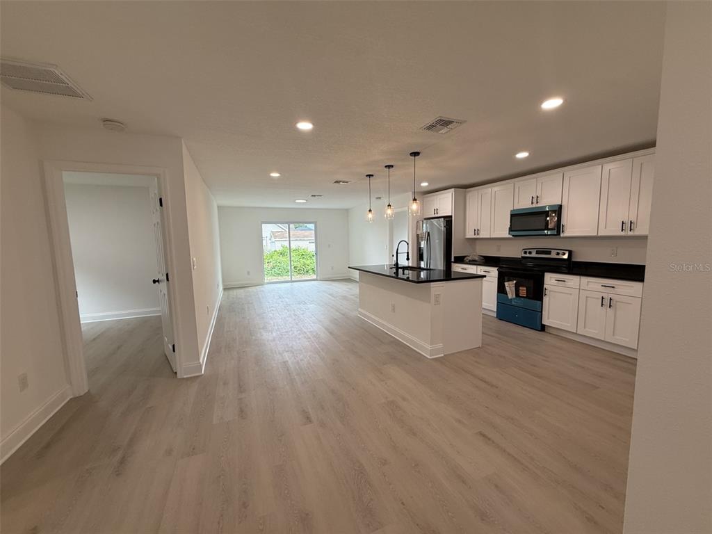 An open-concept kitchen with white cabinets, a central island, and light wood-look flooring — 5400 LAFAYETTE AVENUE, SEBRING, FL