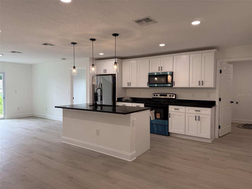 A kitchen features white cabinets, black countertops, a center island, and light-colored wood flooring — 5400 LAFAYETTE AVENUE, SEBRING, FL