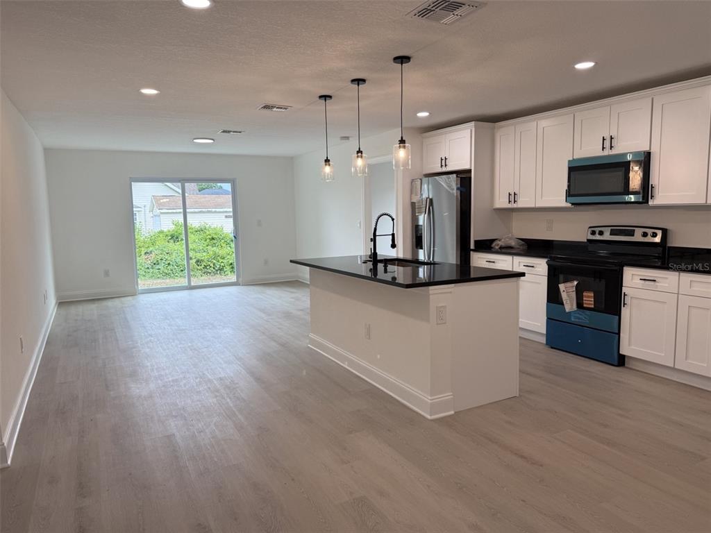 A modern kitchen features white cabinets, a black island countertop, and light wood-look flooring — 5400 LAFAYETTE AVENUE, SEBRING, FL