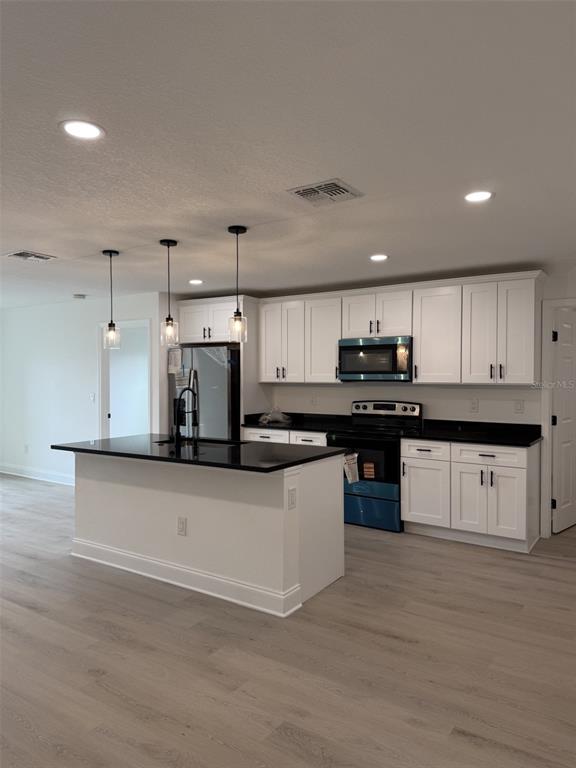 A kitchen features white cabinets, black countertops, a center island, and light wood-look flooring — 5400 LAFAYETTE AVENUE, SEBRING, FL