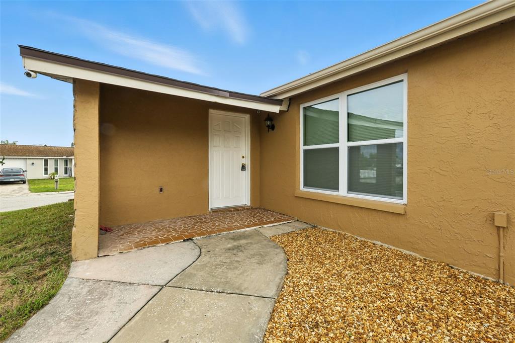 A tan house exterior features a covered entryway, a white front door, and a window — 9239 PALM AVENUE, PORT RICHEY, FL