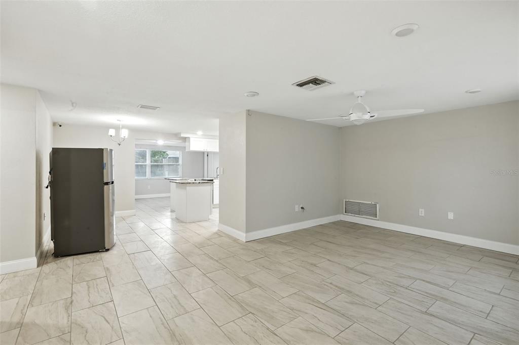 A spacious room with light-colored tile flooring, a ceiling fan, and an adjacent kitchen area — 9239 PALM AVENUE, PORT RICHEY, FL