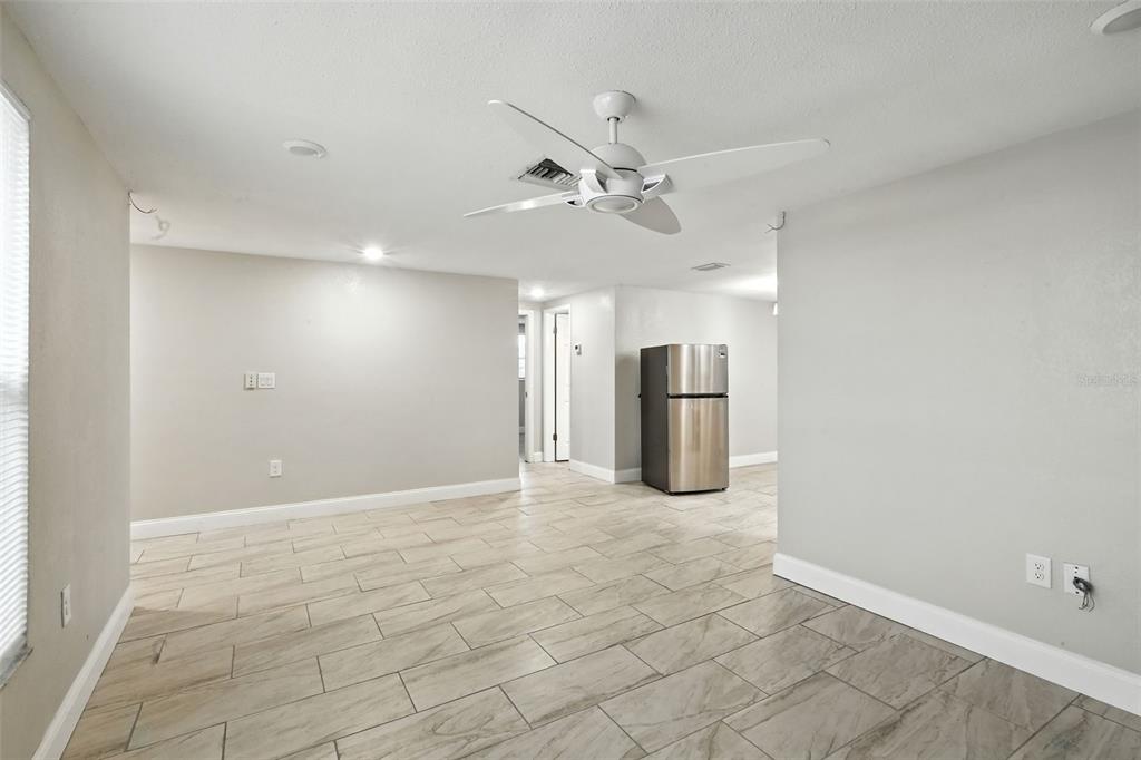 An open-concept room features light gray walls, wood-look tile flooring, and a white ceiling fan — 9239 PALM AVENUE, PORT RICHEY, FL