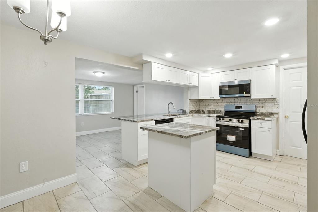A kitchen features white cabinets, a marble-patterned island, stainless steel appliances, and light tile flooring — 9239 PALM AVENUE, PORT RICHEY, FL