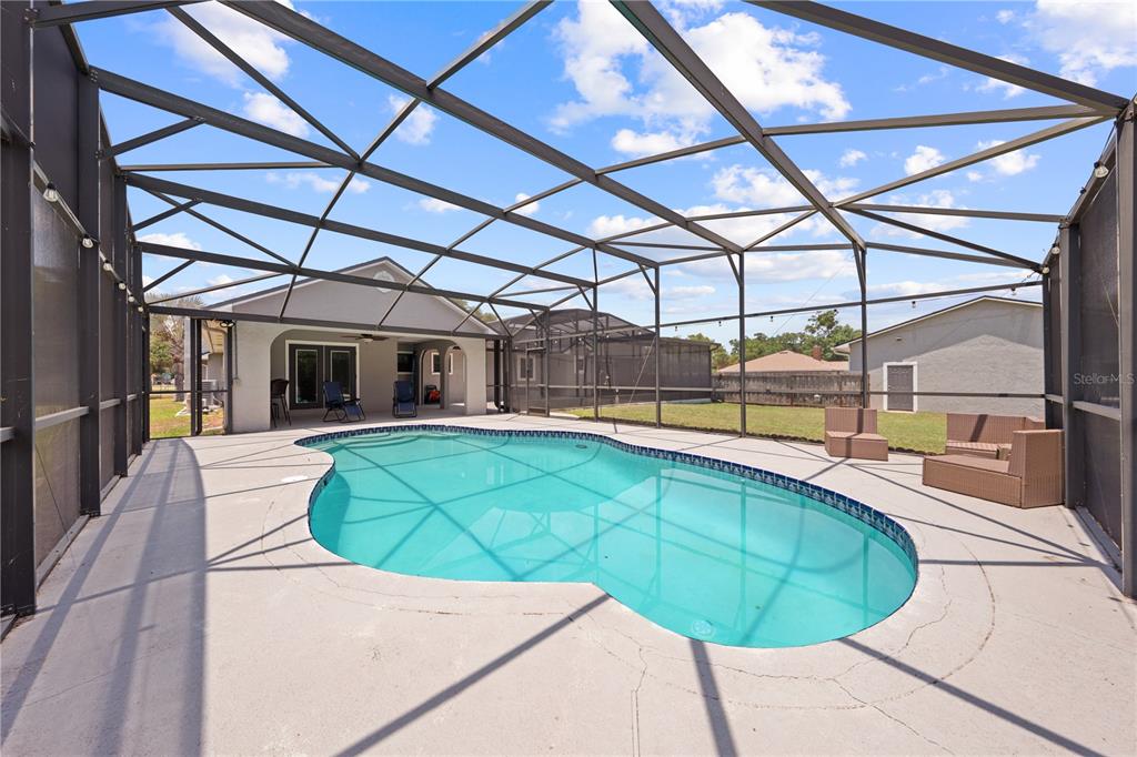 A screened-in patio features a kidney-shaped swimming pool and outdoor furniture on a concrete deck — 233 EASTERN AVENUE, ST CLOUD, FL