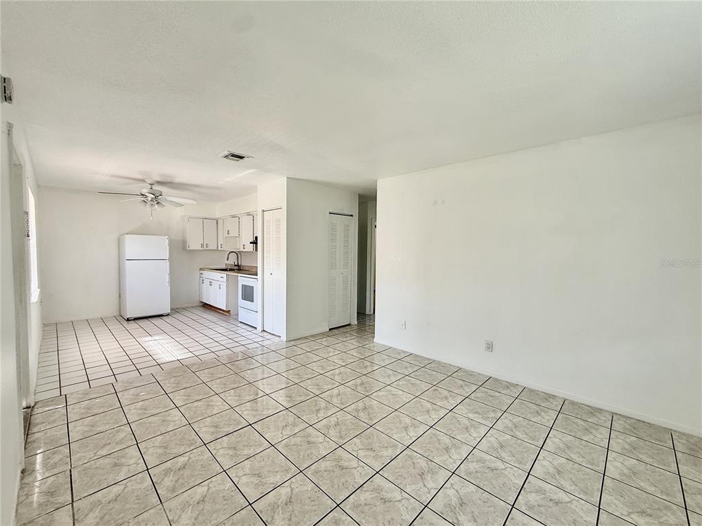 An open-concept room features white walls, a tiled floor, and an adjacent kitchen area — 733 MICHIGAN COURT UNIT 4, ST CLOUD, FL