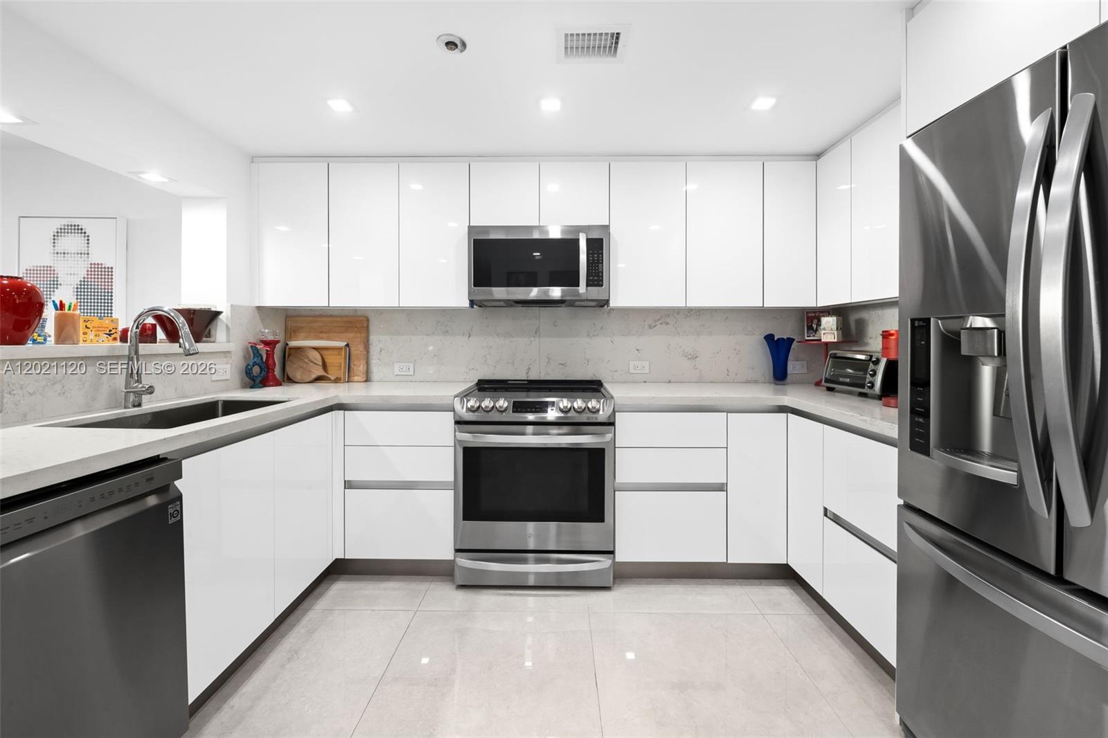 A modern kitchen features white flat-panel cabinets, stainless steel appliances, and light-colored stone countertops — 2555 Collins Ave # 1106, Miami Beach FL 33140, MIAMI BEACH, FL