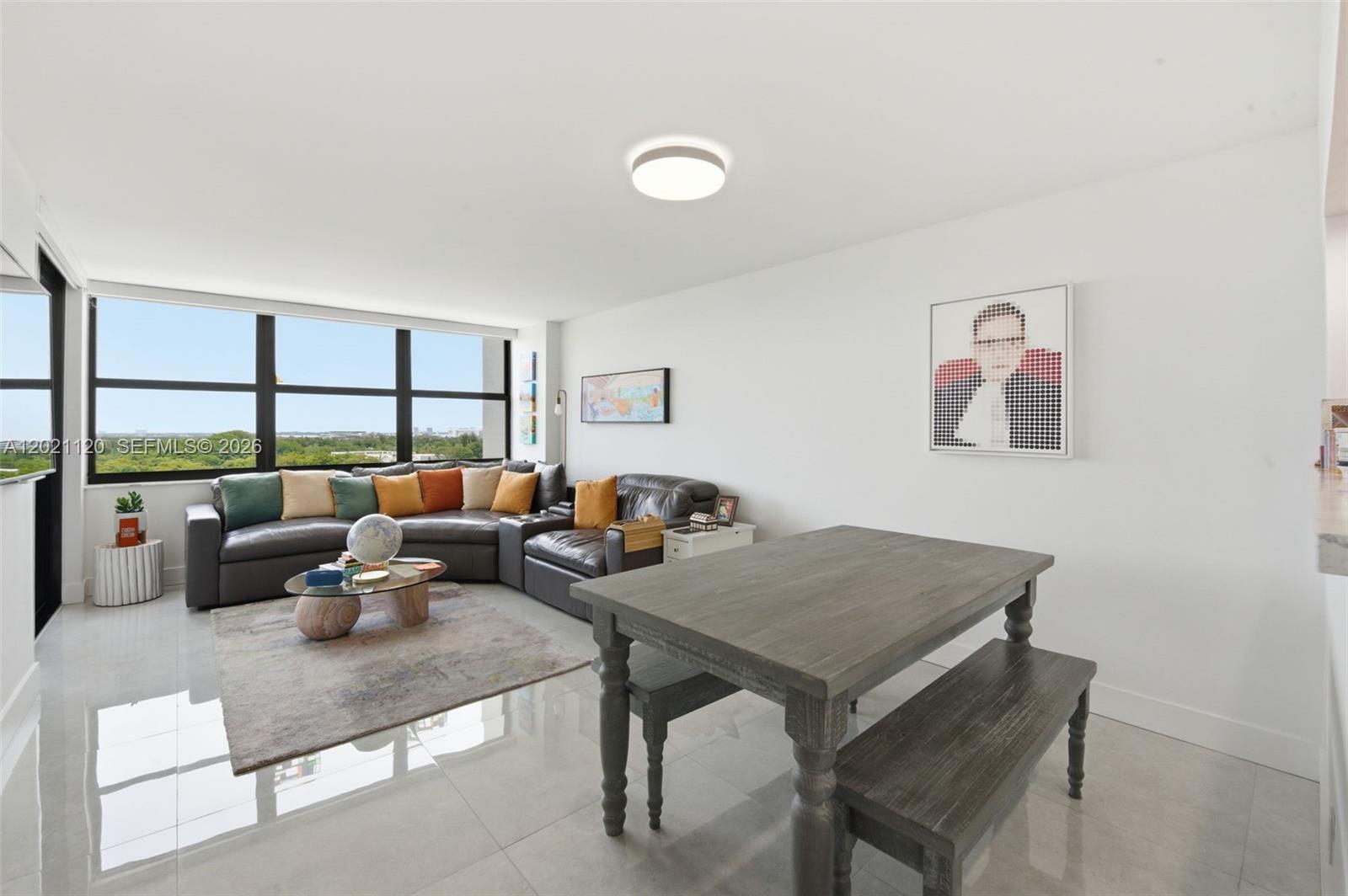 A living and dining area features a sectional sofa, wooden table with benches, and windows — 2555 Collins Ave # 1106, Miami Beach FL 33140, MIAMI BEACH, FL