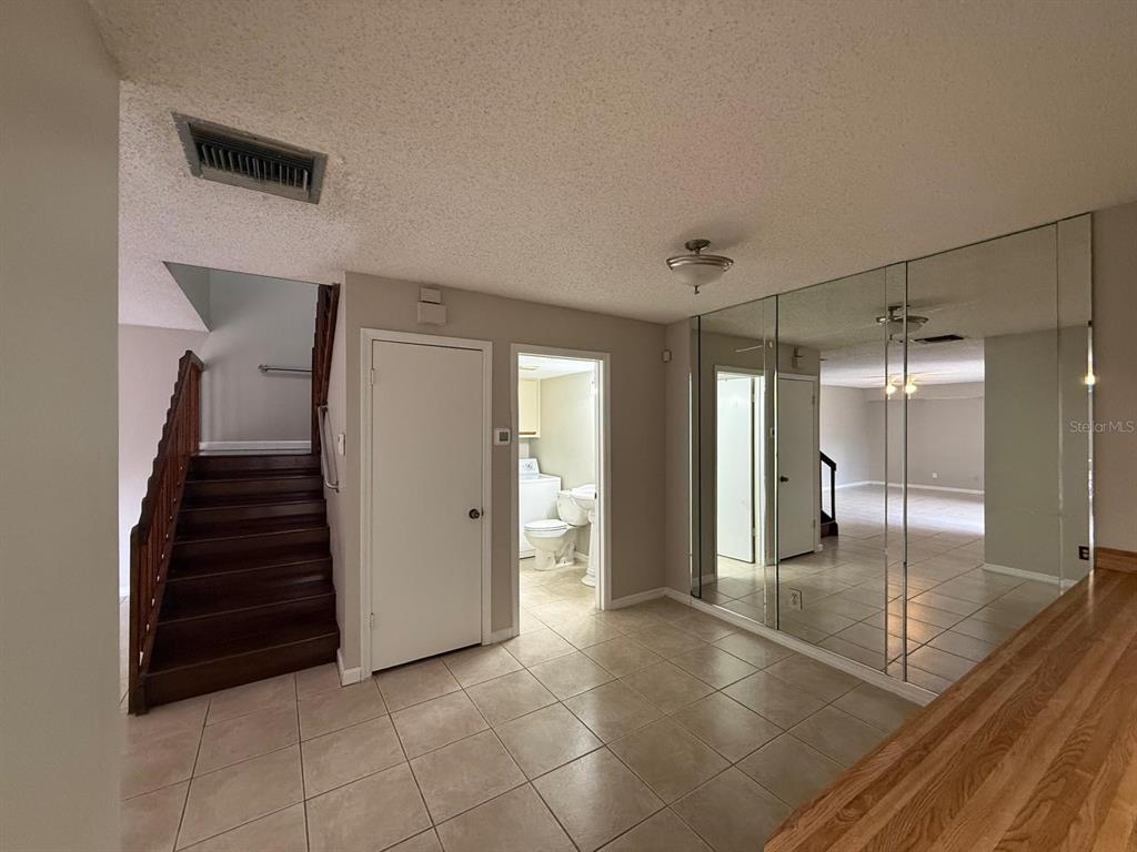 A tiled room features a wooden staircase, a bathroom doorway, and a mirrored wall — 5296 CYPRESS COURT UNIT 433, ORLANDO, FL