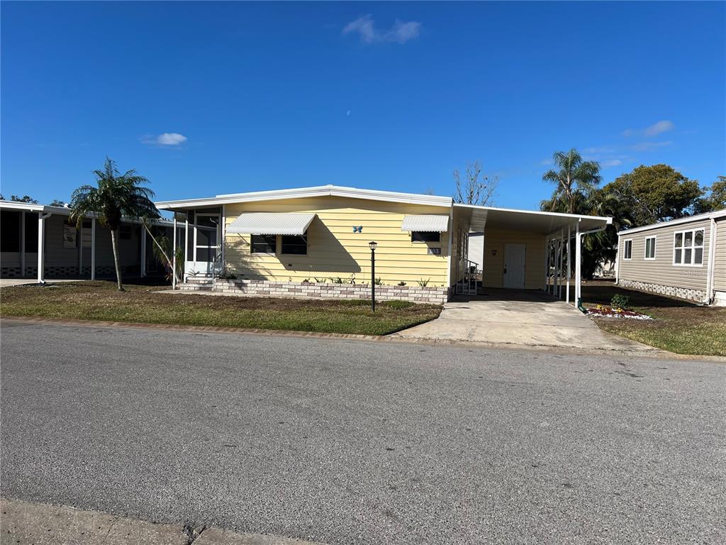 A yellow single-story mobile home with a carport and a small front yard — 6710 36TH AVENUE E UNIT 103, PALMETTO, FL
