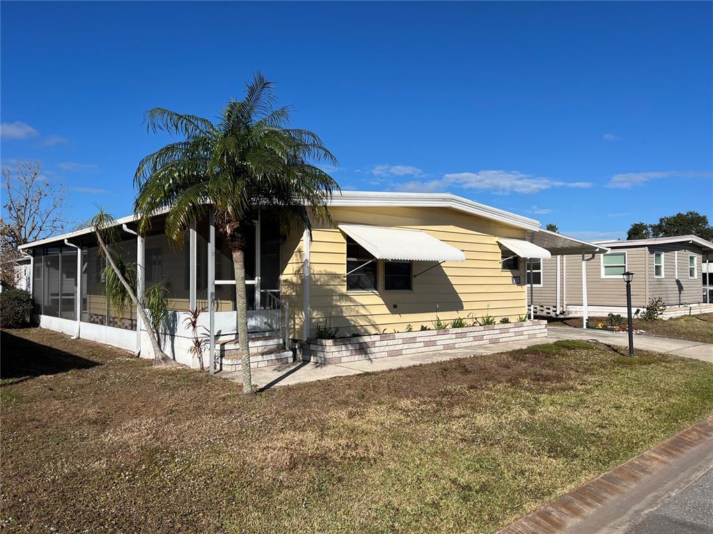 A yellow mobile home features a screened-in porch, a palm tree, and a concrete driveway — 6710 36TH AVENUE E UNIT 103, PALMETTO, FL