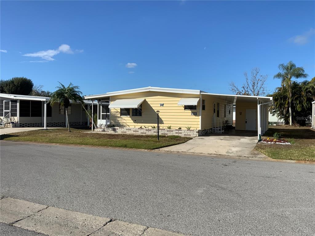 A yellow single-story mobile home features a carport, a brick base, and white awnings — 6710 36TH AVENUE E UNIT 103, PALMETTO, FL