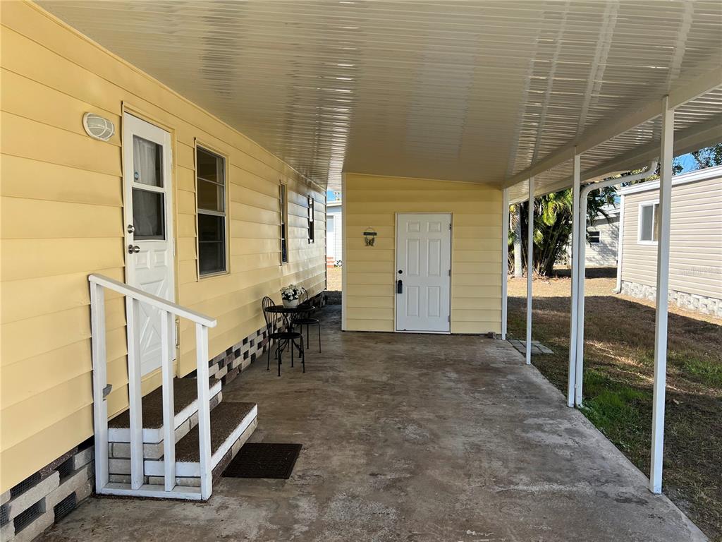 A yellow mobile home exterior features a covered concrete carport and a small staircase — 6710 36TH AVENUE E UNIT 103, PALMETTO, FL