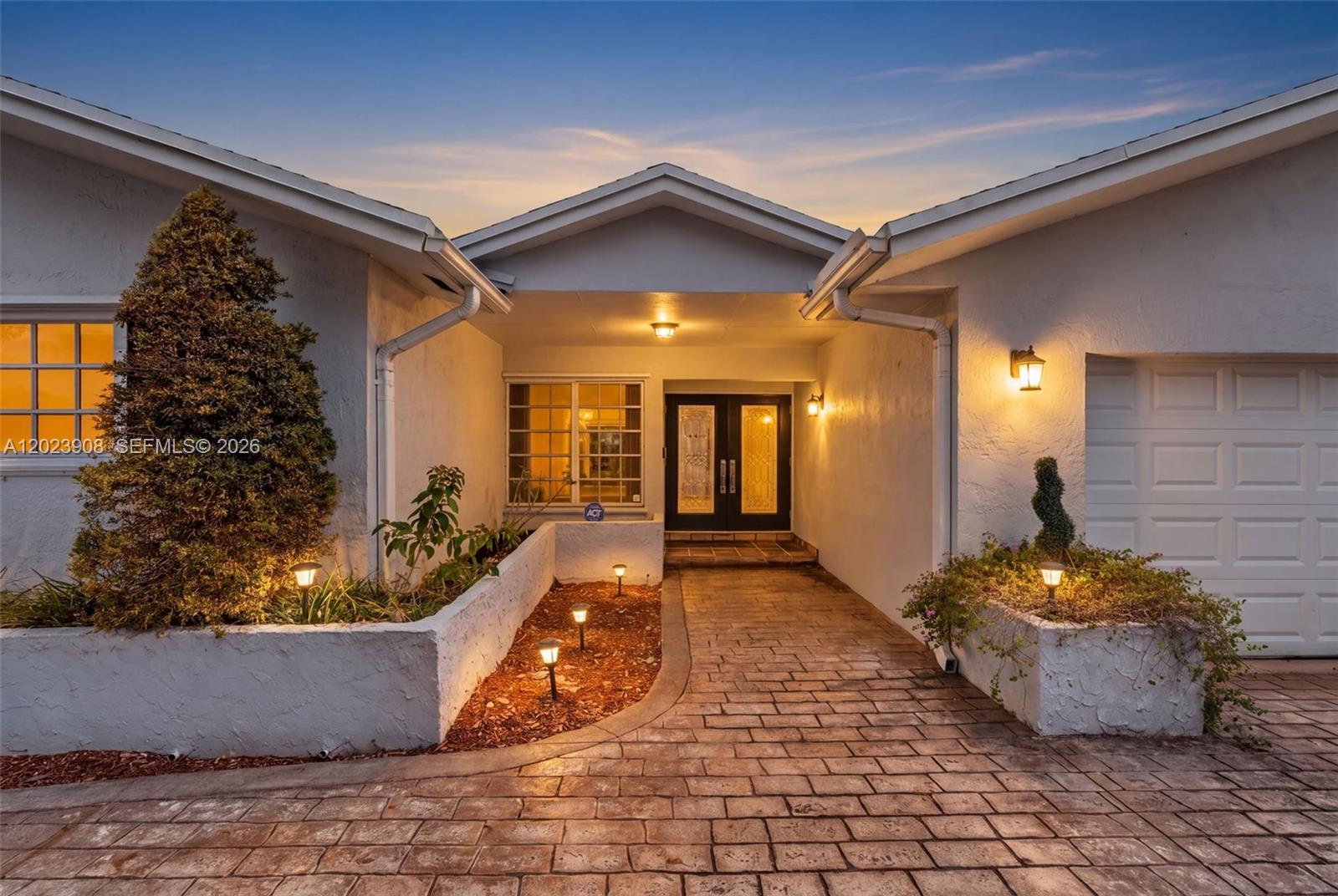 The exterior of a white house features a brick walkway, landscaped planters, and double doors — 14001 SW 108th St, Miami FL 33186, MIAMI, FL