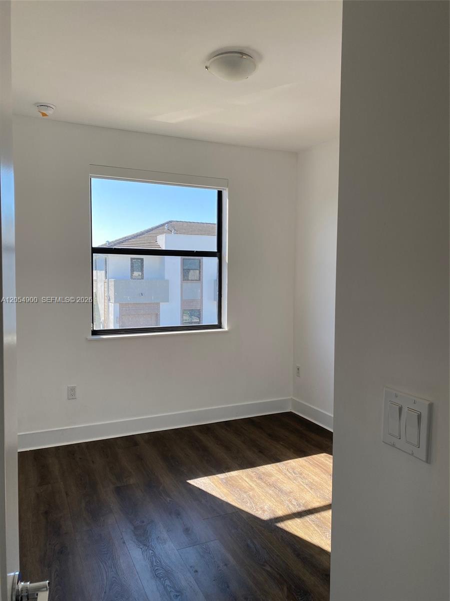 An empty room with white walls, dark wood-look flooring, and a window facing another building — 10602 SW 118th Ave # 10602, Miami FL 33186, MIAMI, FL
