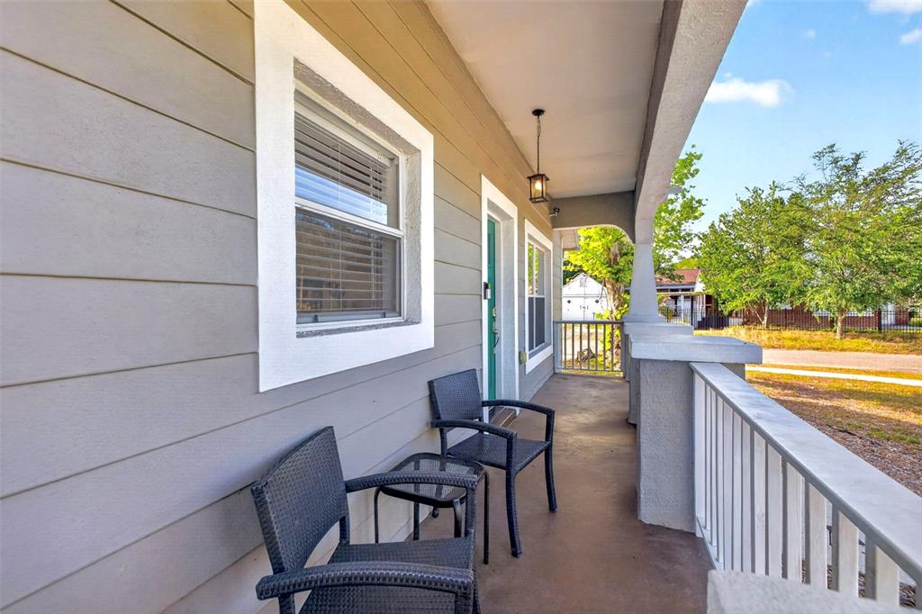 A covered front porch features gray horizontal siding, two black wicker chairs, and a railing — 5801 N MIAMI PLACE, TAMPA, FL