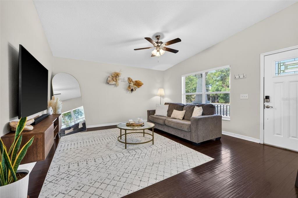 A living room features dark wood floors, a gray sofa, a television, and a large mirror — 5801 N MIAMI PLACE, TAMPA, FL