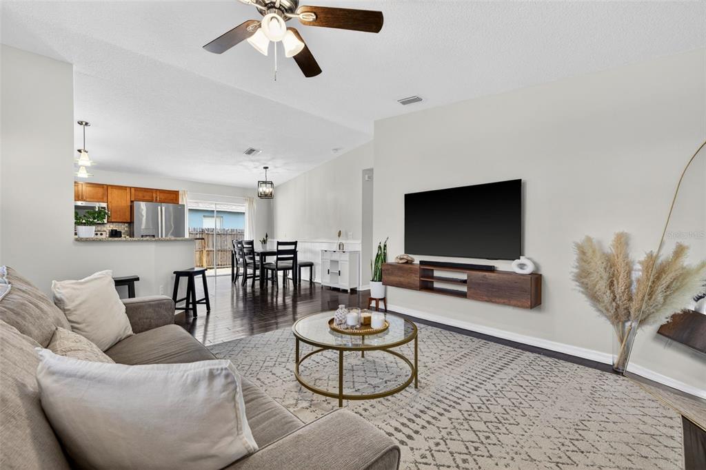 A living room with a wall-mounted television, wood flooring, and an adjacent dining area — 5801 N MIAMI PLACE, TAMPA, FL