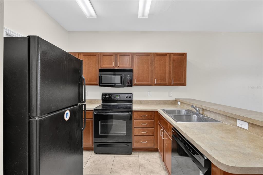 A kitchen features dark wood cabinets, black appliances, and a tan laminate countertop — 2927 SW 35TH PLACE UNIT 115, GAINESVILLE, FL