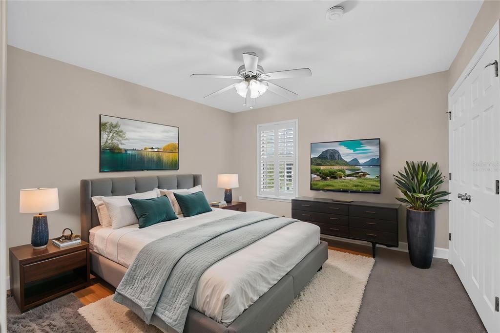 A bedroom features a gray upholstered bed, a dark dresser with a television, and carpet — 2927 SW 35TH PLACE UNIT 115, GAINESVILLE, FL