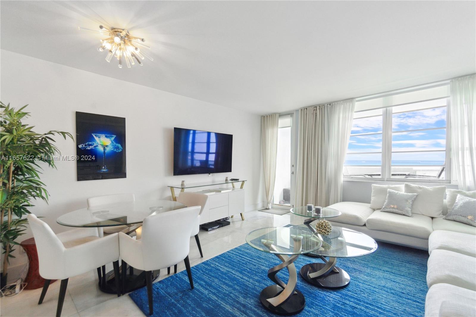 A bright living and dining area features white furniture, a blue rug, and ocean views — 100 Lincoln Rd # 1534, Miami Beach FL 33139, MIAMI BEACH, FL