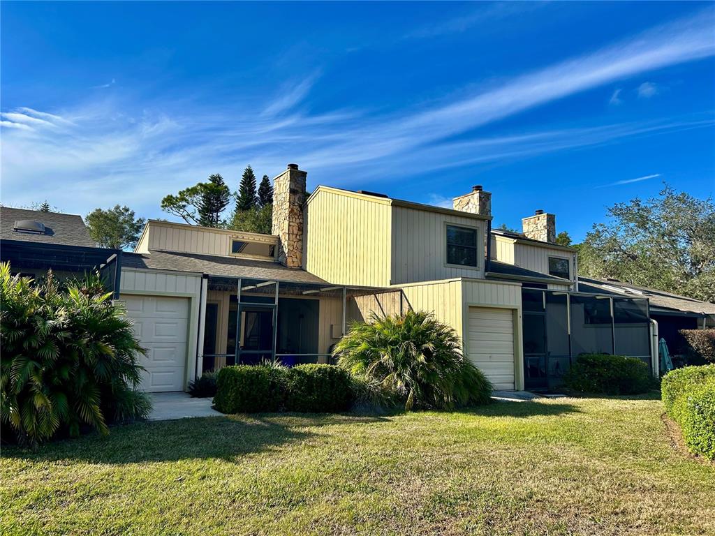 The exterior of a multi-level townhouse features light-colored vertical siding, stone chimneys, and screened-in patios — 19 ASPEN DR. UNIT 19, HAINES CITY, FL