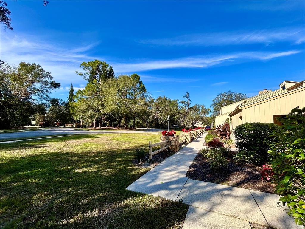 A concrete walkway leads past a stone planter and wooden fence toward a tan building — 19 ASPEN DR. UNIT 19, HAINES CITY, FL