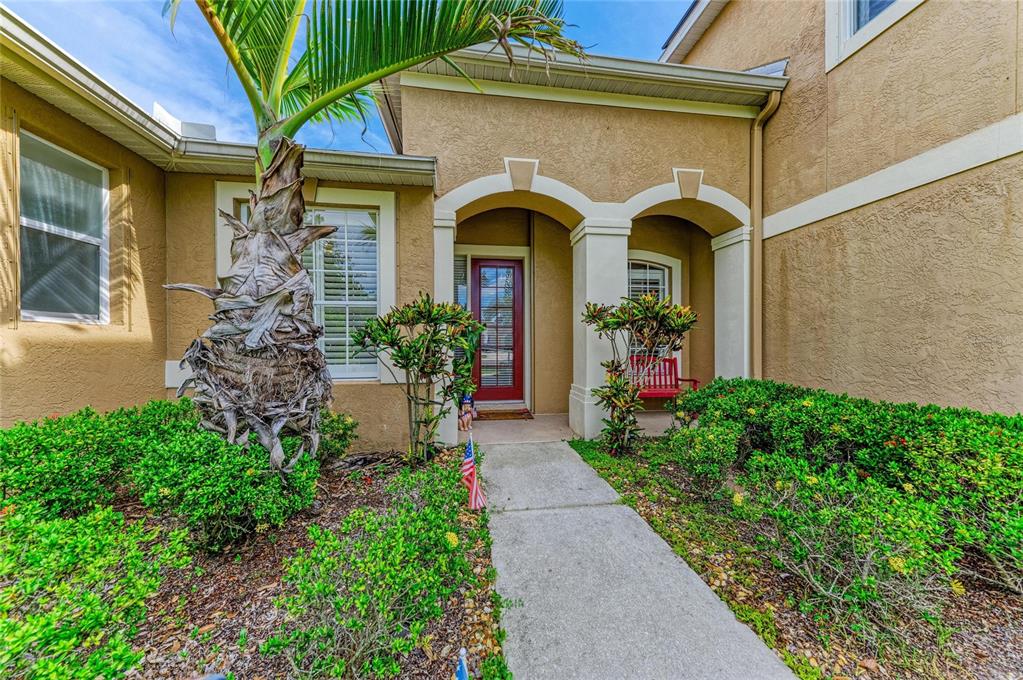 A tan stucco house exterior features a red front door, arched entryway, and landscaping — 10918 BULLRUSH TERRACE, LAKEWOOD RANCH, FL