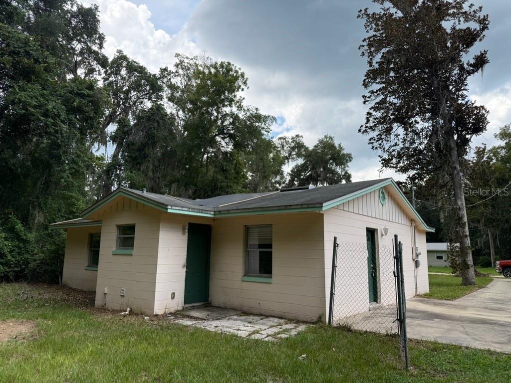 A single-story house with light-colored siding, a green door, and a chain-link fence — 107 WOODLAWN ROAD, SATSUMA, FL