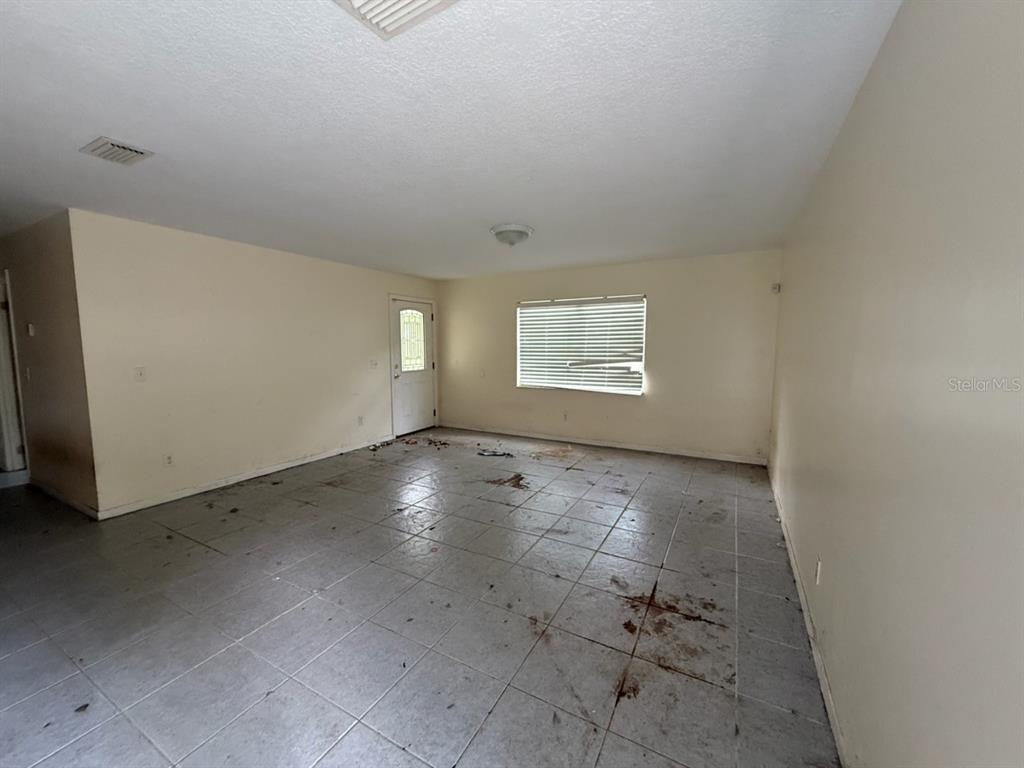 An empty room with light-colored walls, a tiled floor, a window, and a door — 107 WOODLAWN ROAD, SATSUMA, FL