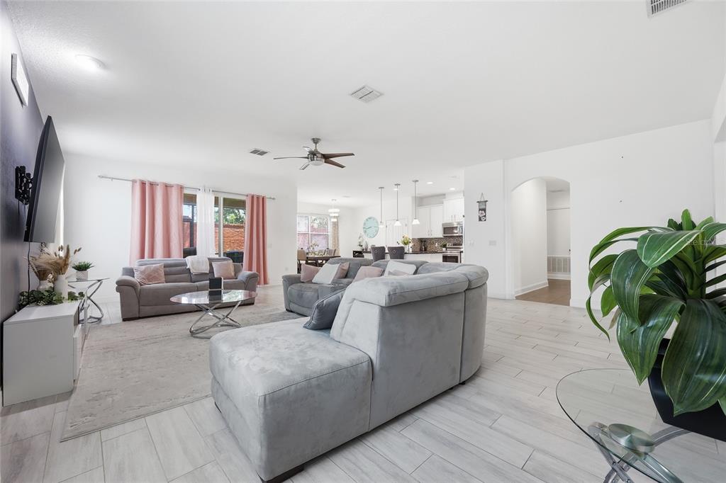 A spacious open-concept living room features light tile flooring, gray sectional sofas, and a kitchen — 3316 MCCORMICK WOODS DRIVE, OCOEE, FL