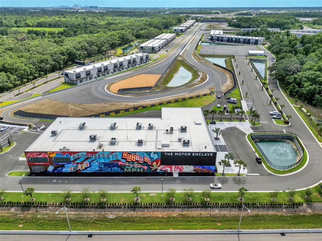 An aerial view shows a large building with a mural next to a racetrack facility — 6500 MOTOR ENCLAVE WAY UNIT 1214, TAMPA, FL