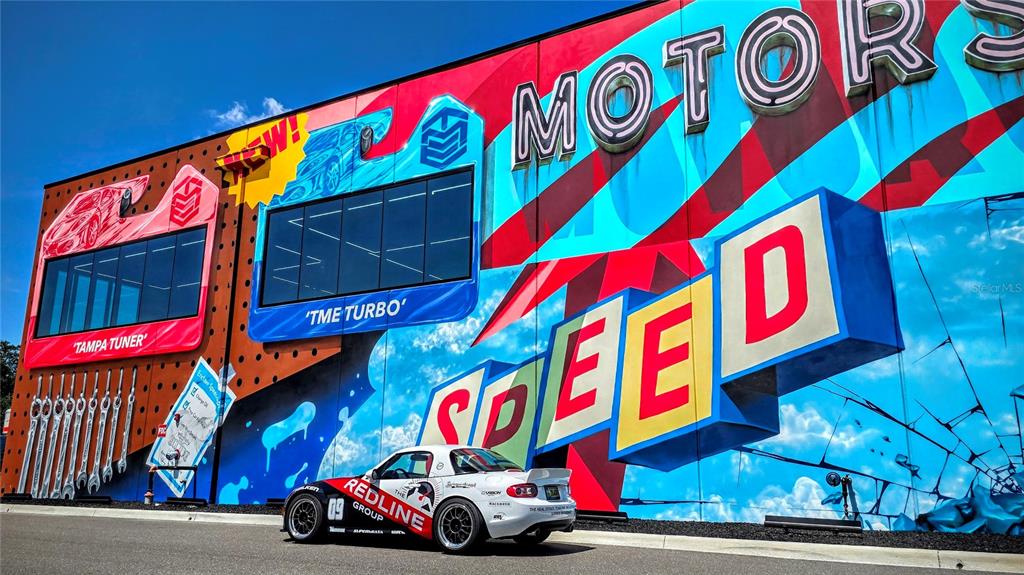 A white sports car is parked in front of a building with colorful mural walls — 6500 MOTOR ENCLAVE WAY UNIT 1214, TAMPA, FL