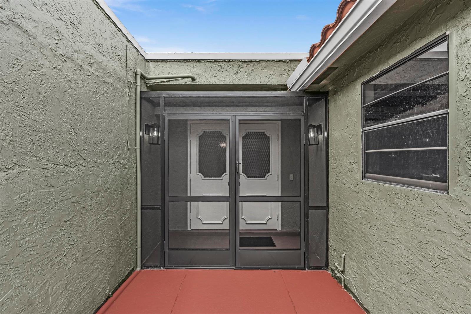 A screened-in entryway with double doors sits between two stucco walls on a red patio — 5463 Alta Way, Lake Worth FL 33467, LAKE WORTH, FL