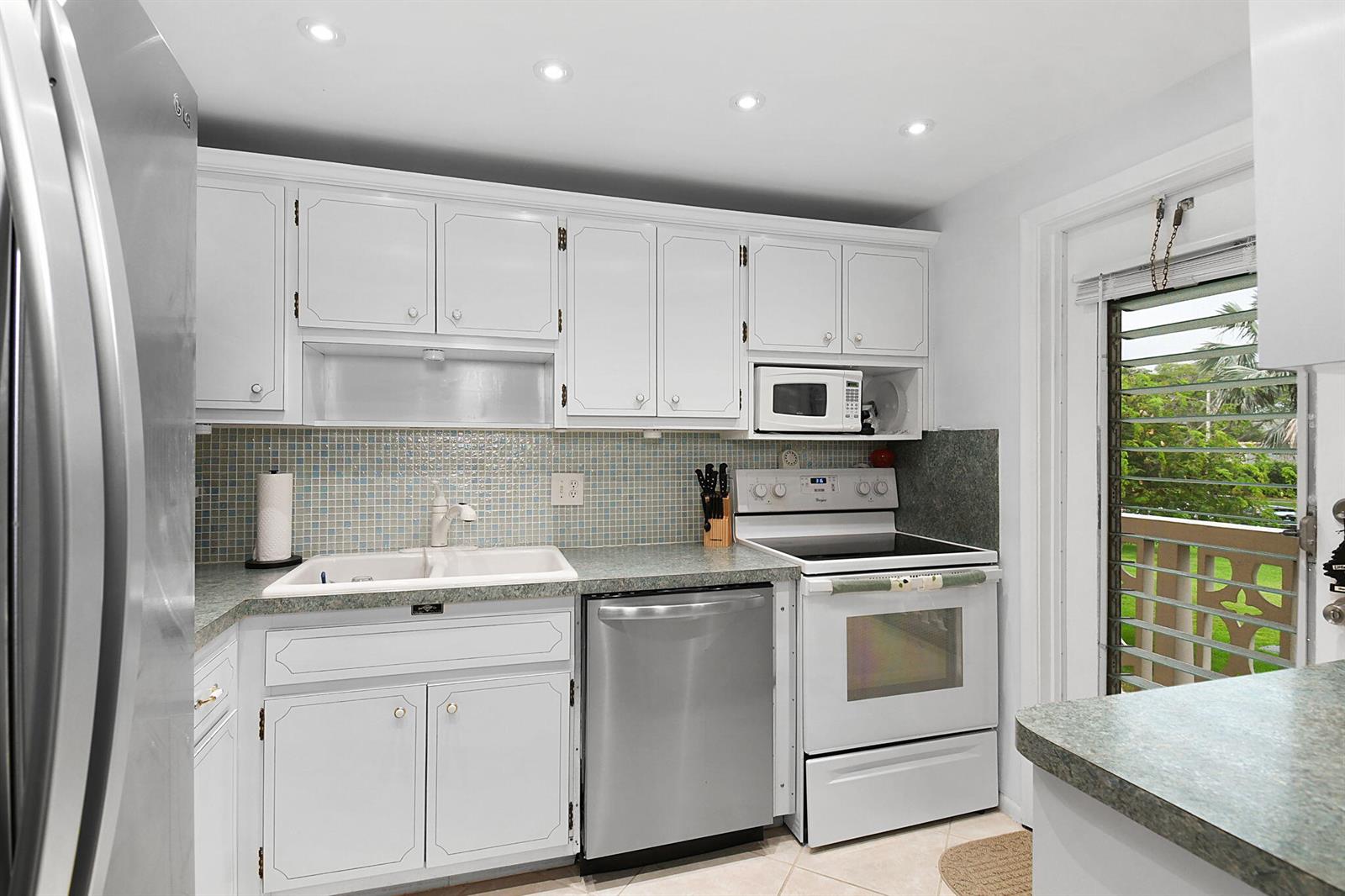 A kitchen with white cabinets, stainless steel appliances, a tiled backsplash, and a balcony door — 400 NE 20th Street # A207, Boca Raton FL 33431, BOCA RATON, FL