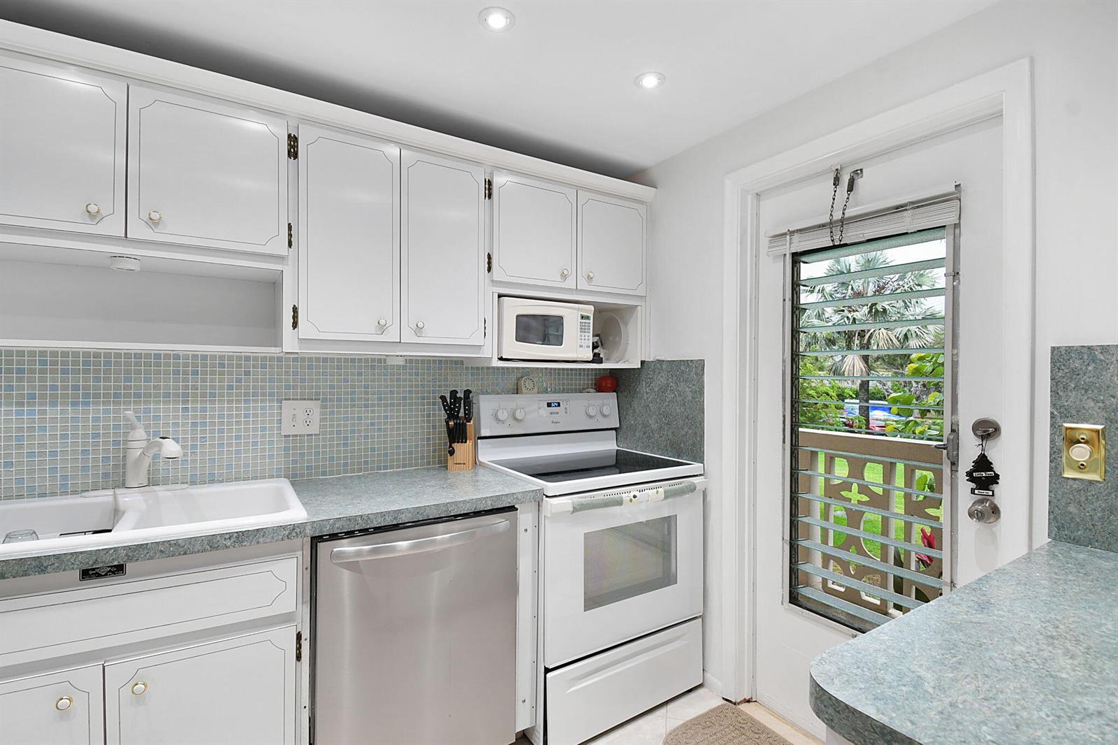 A kitchen with white cabinets, a stainless steel dishwasher, a white stove, and a glass door — 400 NE 20th Street # A207, Boca Raton FL 33431, BOCA RATON, FL