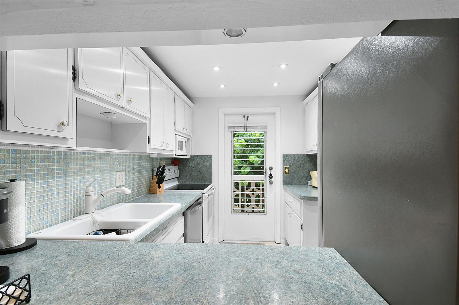 A kitchen features white cabinets, blue countertops, a tiled backsplash, and a glass-paned door — 400 NE 20th Street # A207, Boca Raton FL 33431, BOCA RATON, FL