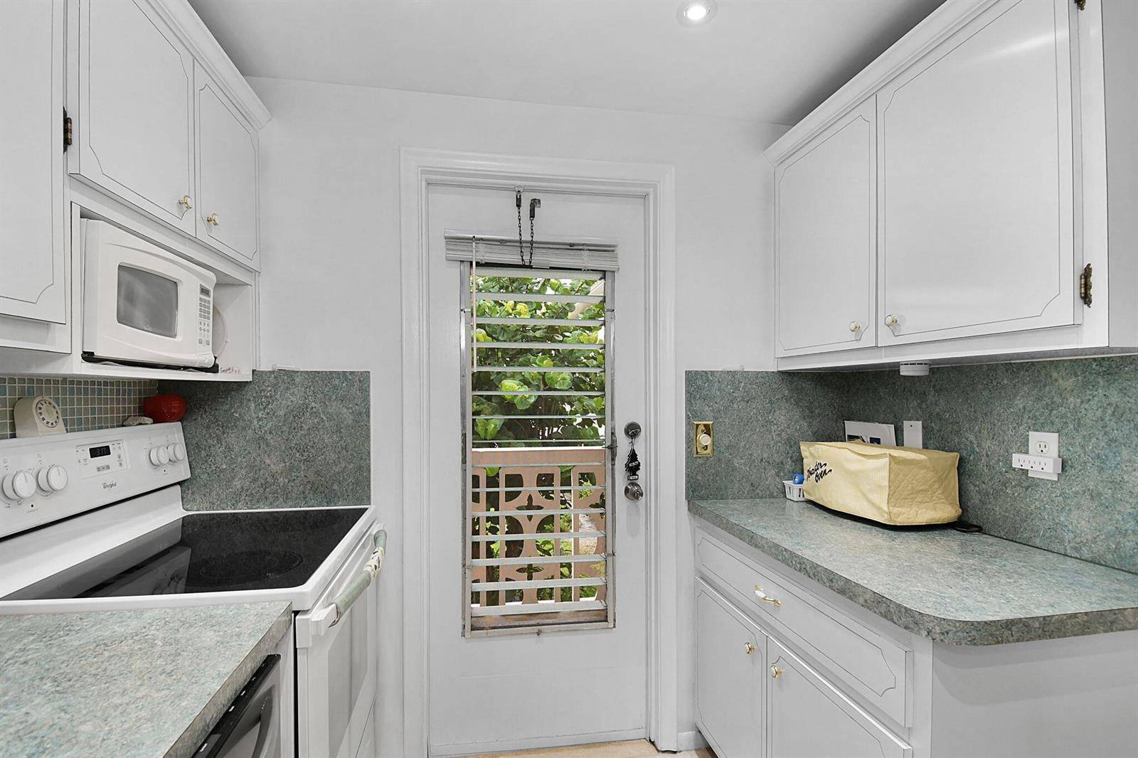 A kitchen with white cabinets, a glass-top stove, a microwave, and a door with shutters — 400 NE 20th Street # A207, Boca Raton FL 33431, BOCA RATON, FL