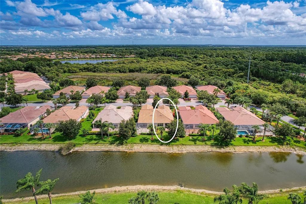 An aerial view of a suburban neighborhood featuring a house circled in white near a pond — 6083 BENEVENTO DRIVE, SARASOTA, FL