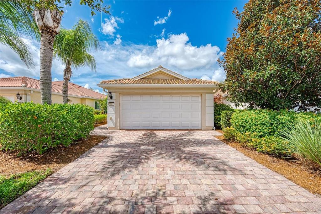 A paved driveway leads to the white garage door of a single-story suburban house — 6083 BENEVENTO DRIVE, SARASOTA, FL
