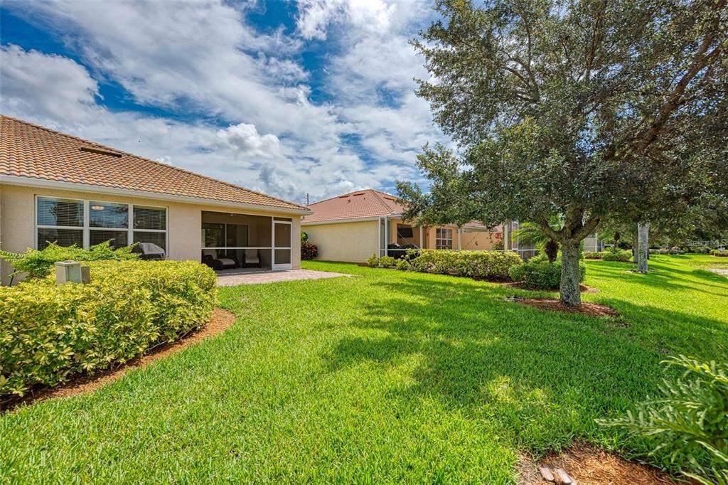 The backyard features a grassy lawn, a paved patio, and a screened-in porch area — 6083 BENEVENTO DRIVE, SARASOTA, FL