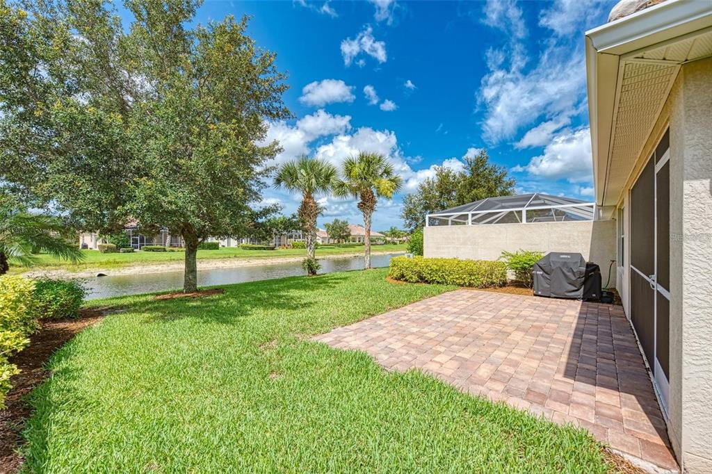 A paved patio sits beside a house with a screened enclosure overlooking a small pond — 6083 BENEVENTO DRIVE, SARASOTA, FL