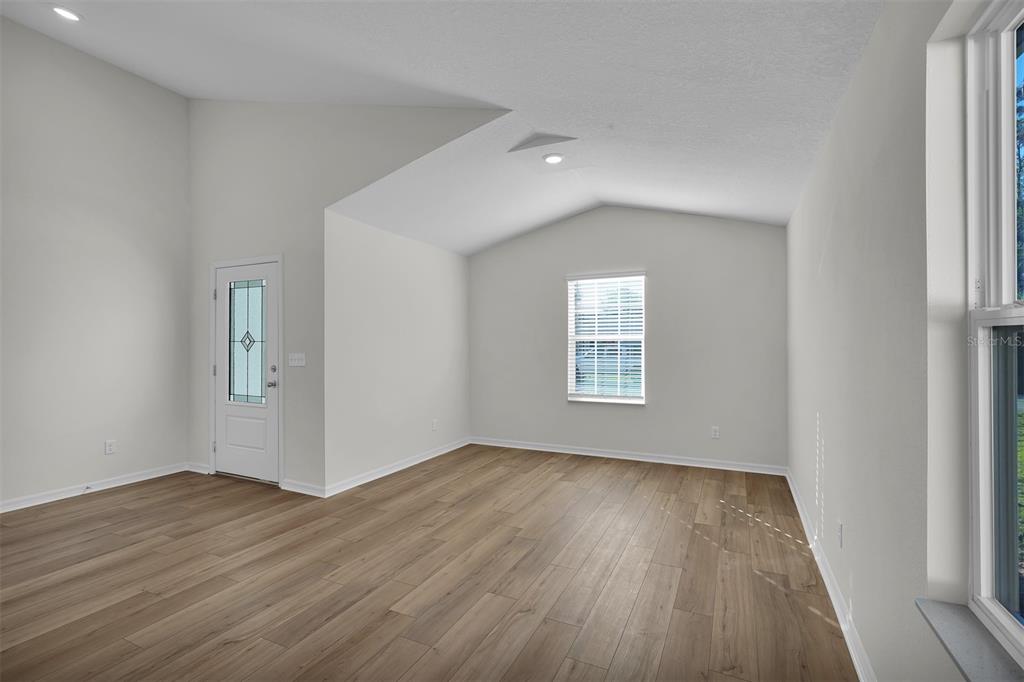 An empty room with light wood-look flooring, white walls, a vaulted ceiling, and a door — 48 PRATTWOOD LANE, PALM COAST, FL