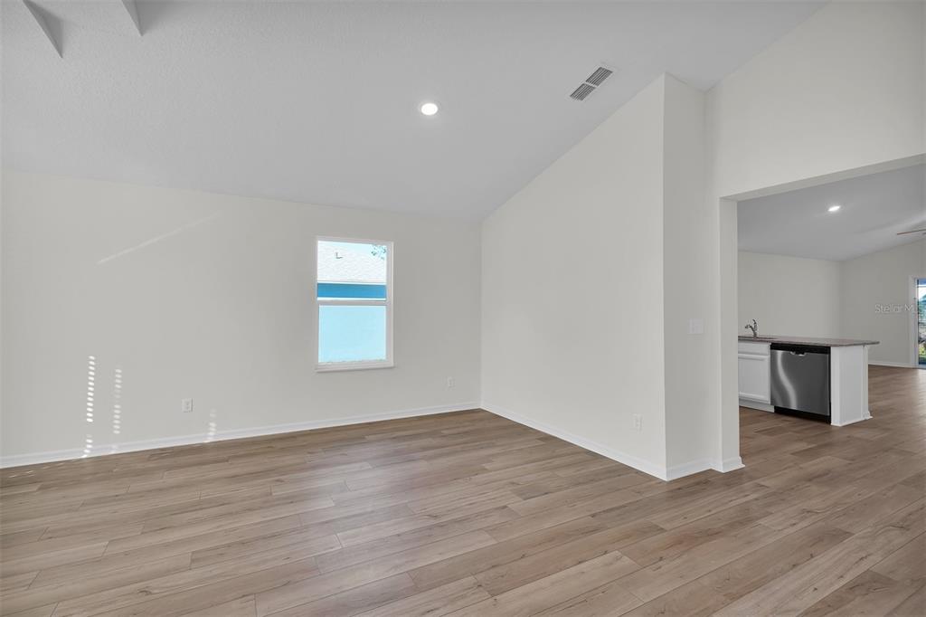 A bright living room with light wood-look flooring and a view into the kitchen — 48 PRATTWOOD LANE, PALM COAST, FL