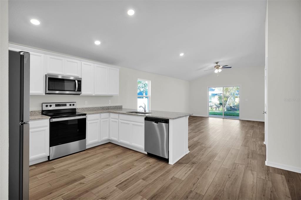 A kitchen with white cabinets, stainless steel appliances, and granite countertops opens to a living area — 48 PRATTWOOD LANE, PALM COAST, FL