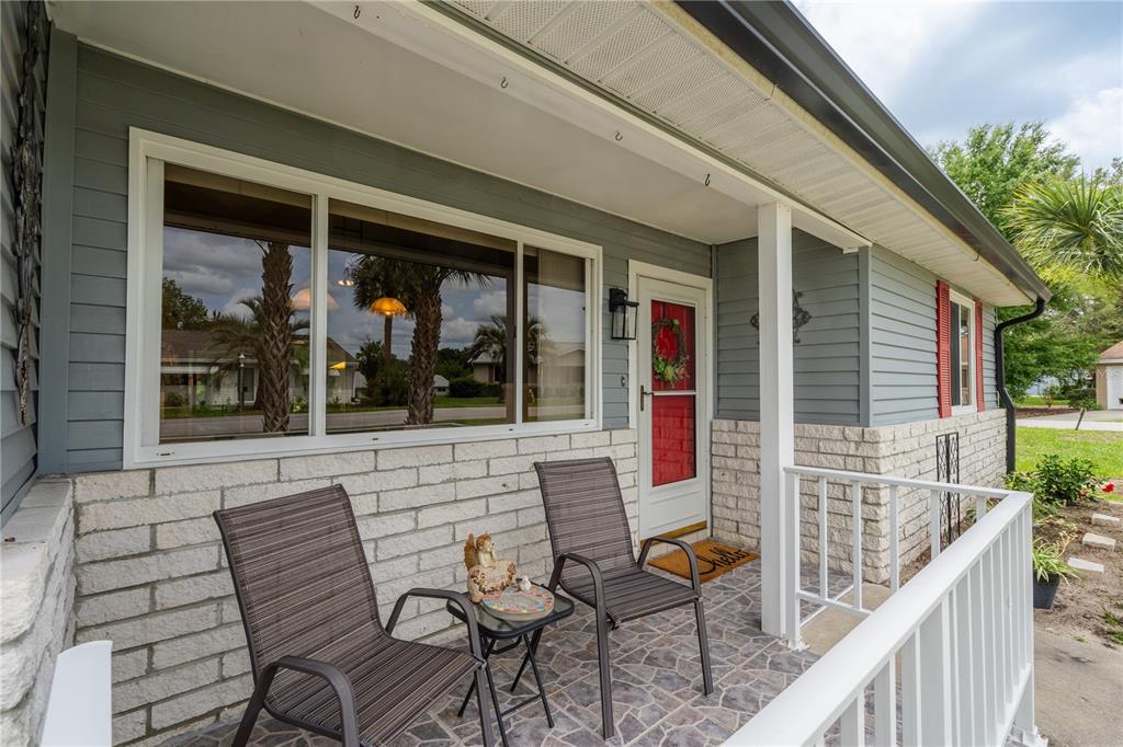A covered front porch features gray siding, white brick, two chairs, and a red door — 10839 SW 87TH TERRACE, OCALA, FL