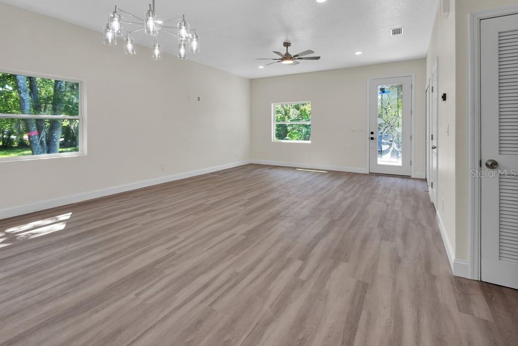 An empty living room features light wood-look flooring, a ceiling fan, and a modern chandelier — 556 WALLACE STREET, DAYTONA BEACH, FL