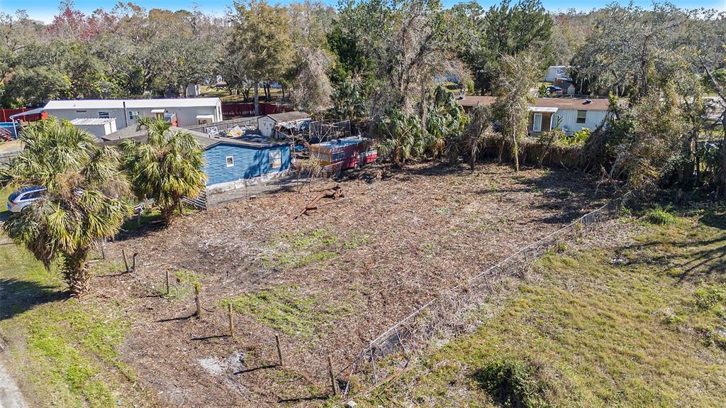 An elevated view of a cleared, fenced residential lot with surrounding trees and nearby mobile homes — POLO STREET, NEW PORT RICHEY, FL