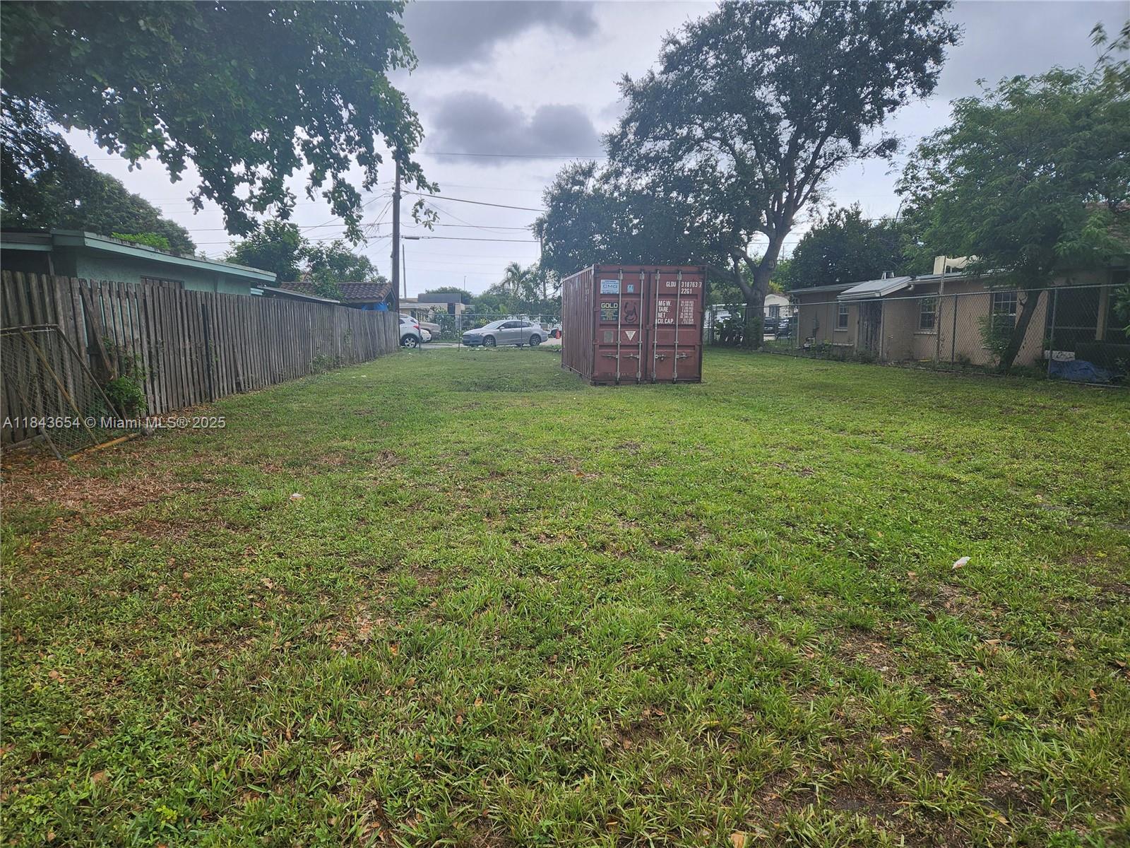 A large, grassy backyard features a brown shipping container and is enclosed by wooden fencing — 315 N 61st Ave, Hollywood FL 33024, HOLLYWOOD, FL